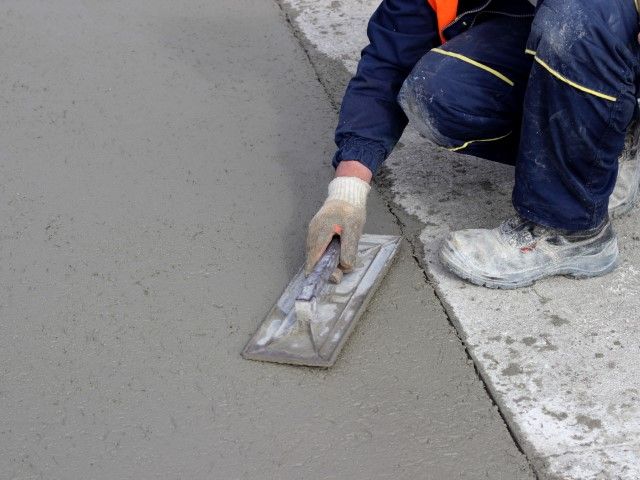 Worker smoothing wet concrete with a trowel on a sidewalk edge