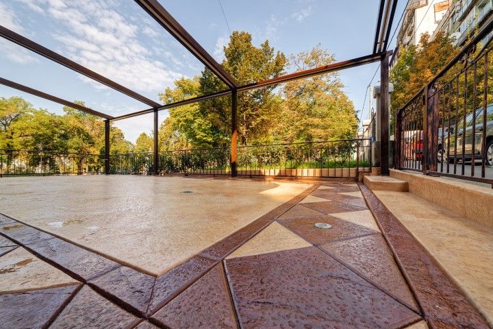 Empty outdoor patio with geometric stone floor, pergola frame, and trees in the background