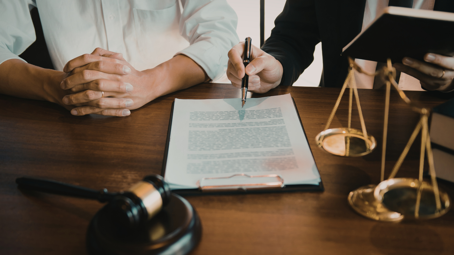 A lawyer pointing to a document on a desk with a gavel and balance scale nearby, representing legal consultation.