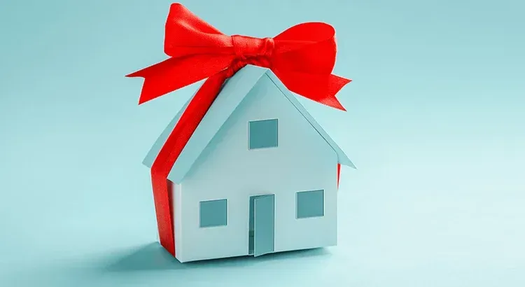 a small white house wrapped in a red ribbon with a bow .