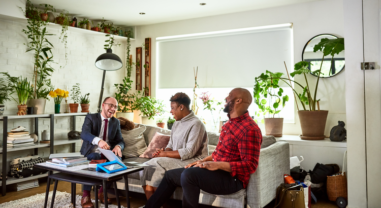 a group of people are sitting on a couch in a living room talking to each other .