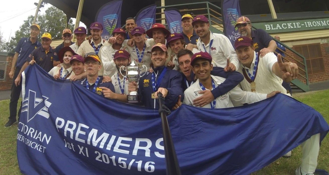 Cricket team posing with a championship trophy and blue “Premiers 2015/16” banner