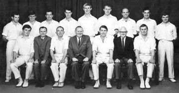 Black-and-white group portrait of 14 people posed in two rows, seated and standing in formal attire