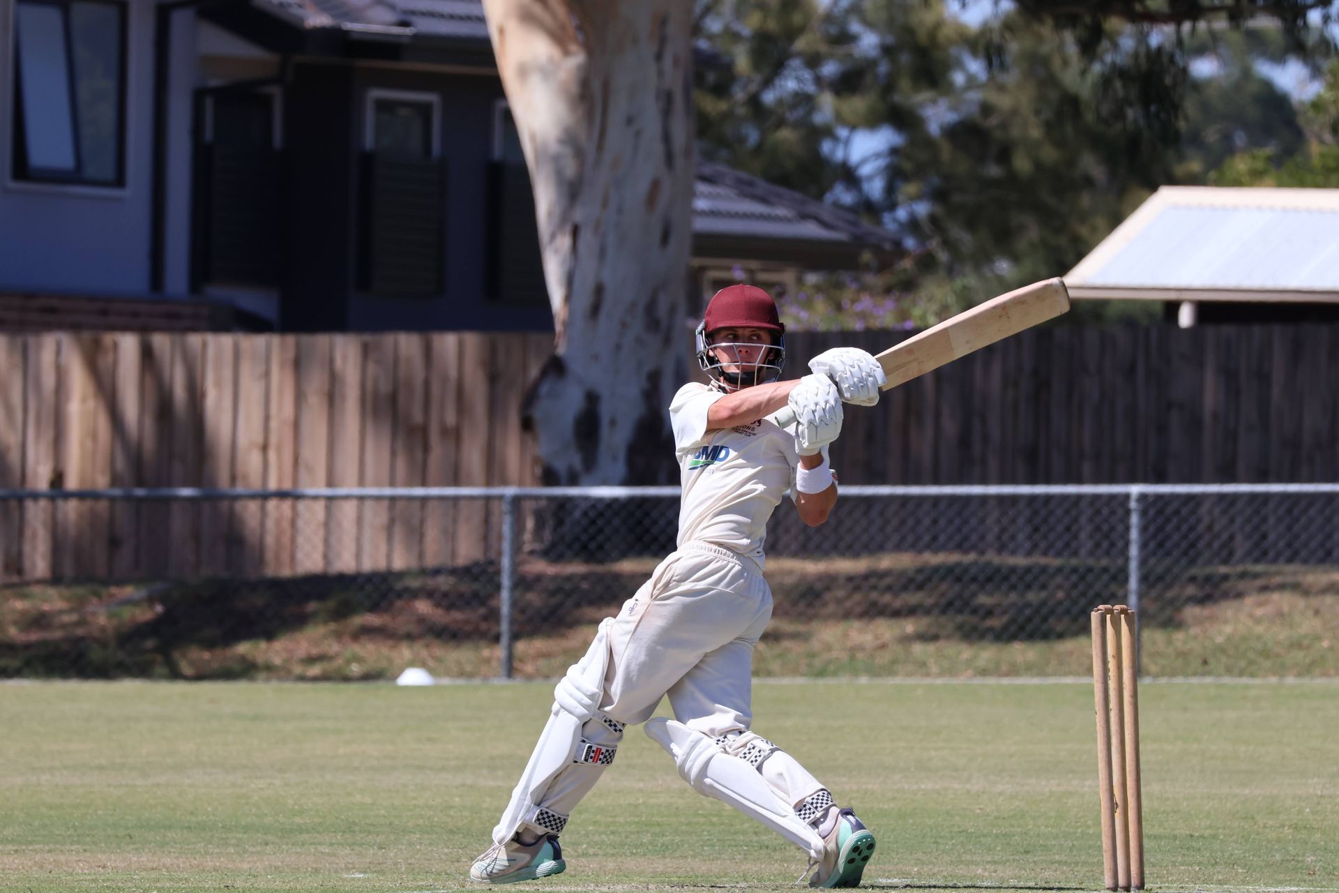 Cricketer in white uniform swinging a bat on a grassy field during a match