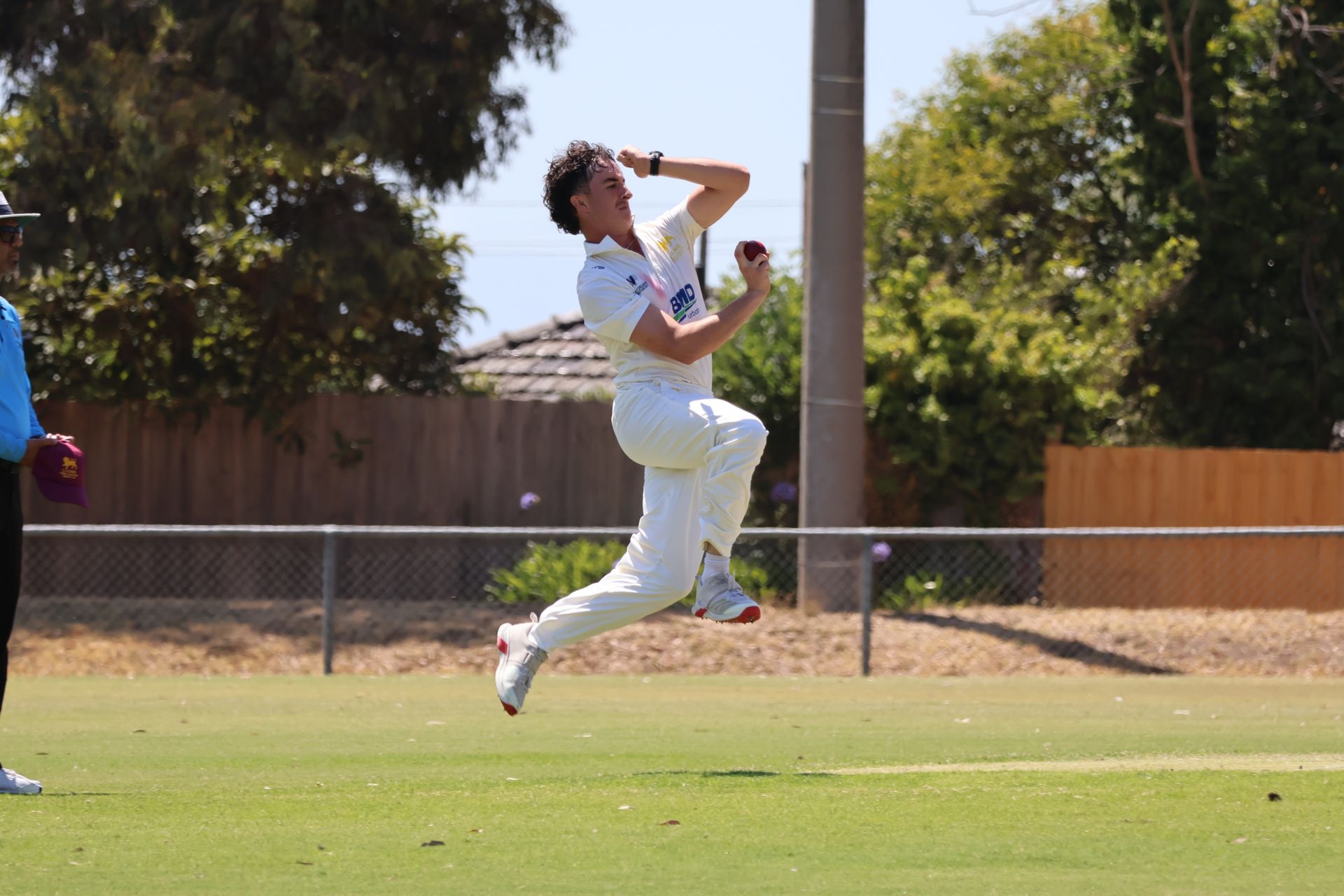 Cricketer in white uniform leaping to catch a ball on a sunny field