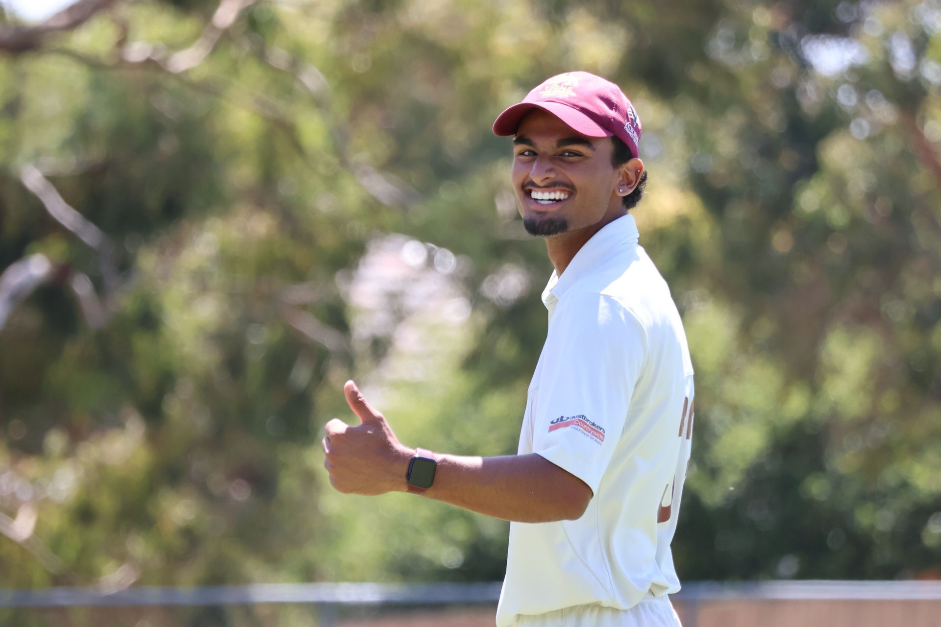 Smiling golfer in a maroon cap giving a thumbs-up on a sunny course