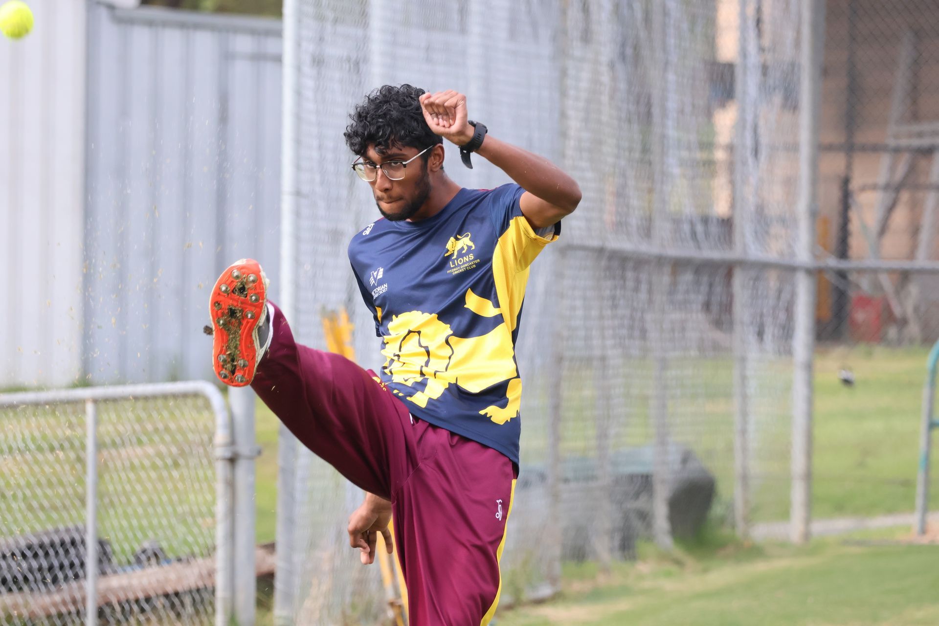 Soccer player in blue and yellow jersey kicking high near a chain-link fence