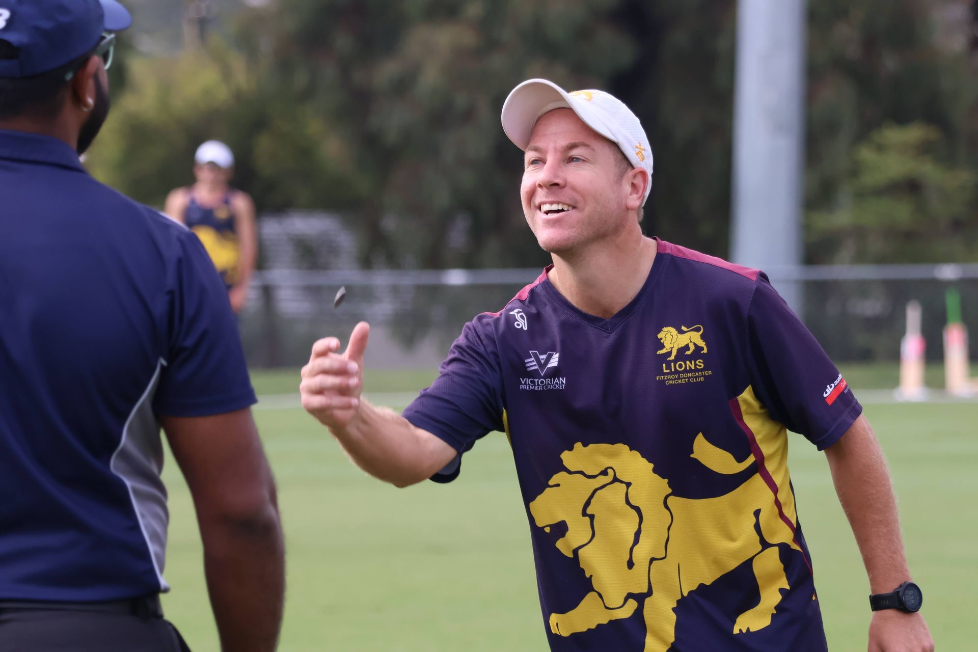 Man in purple and yellow sports shirt smiling and gesturing on a grassy field during practice