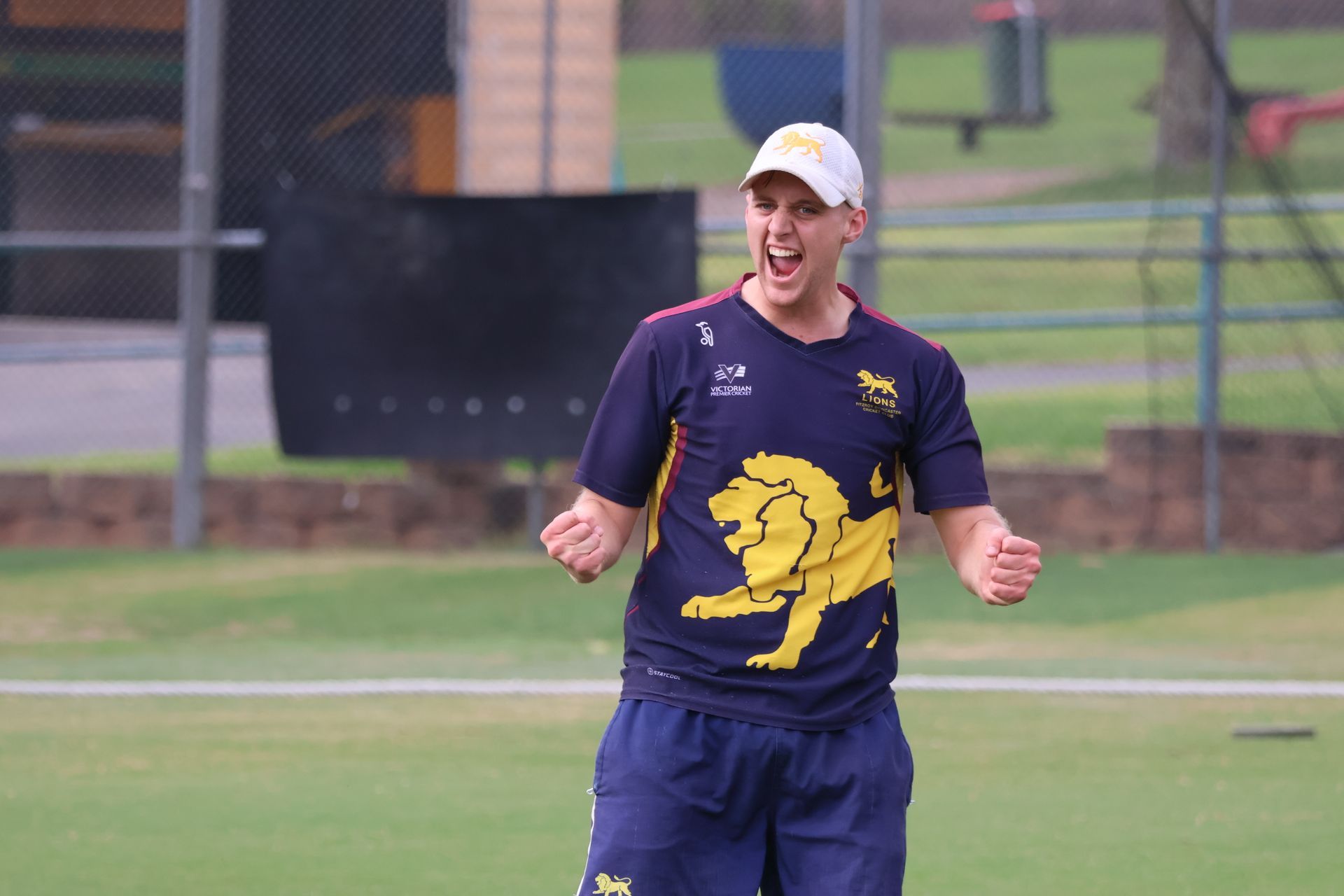 Cricket player in navy and gold uniform celebrating on a practice field with raised fists