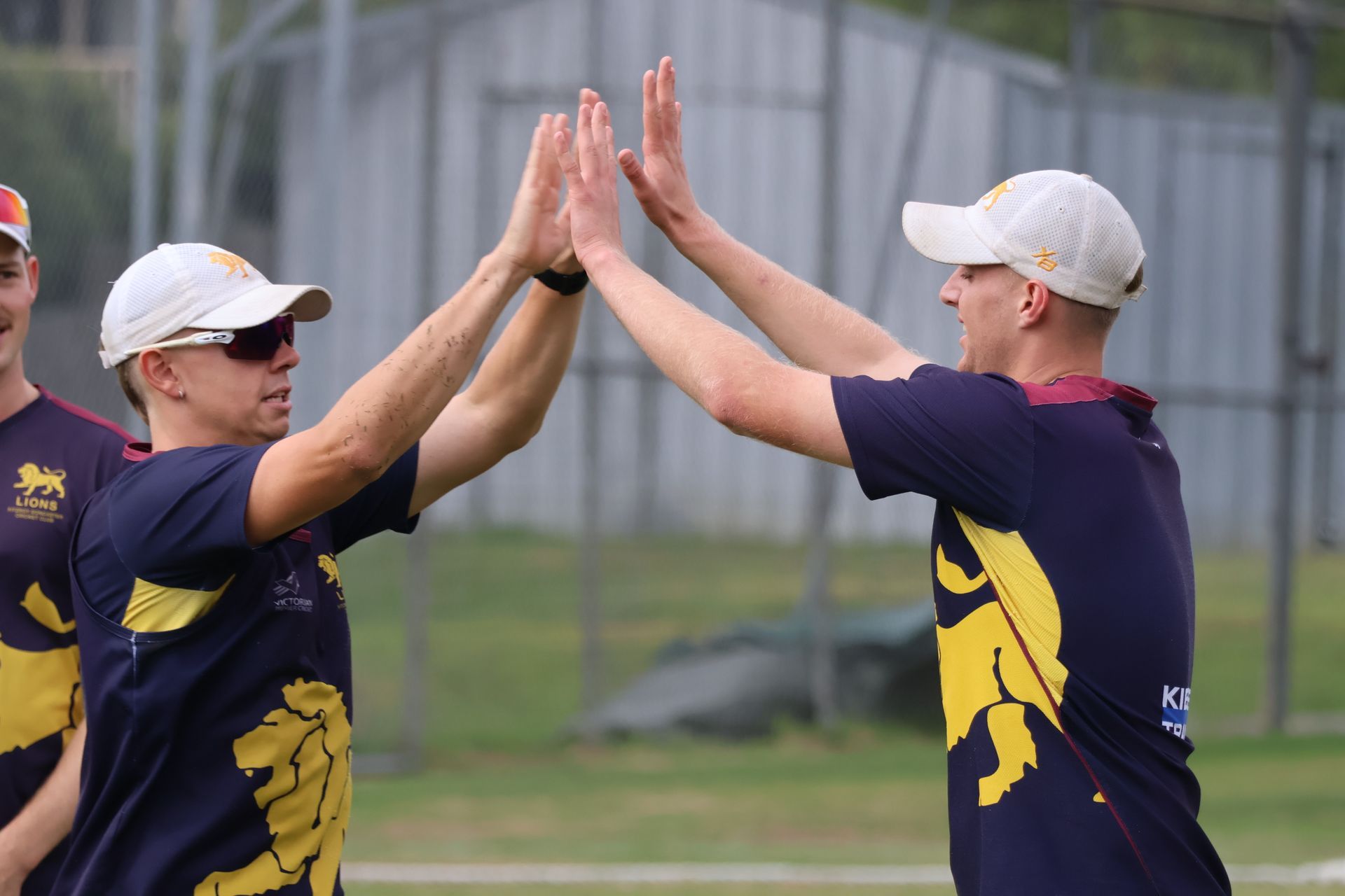 Two athletes in navy and yellow uniforms high-five on a field, smiling during practice.