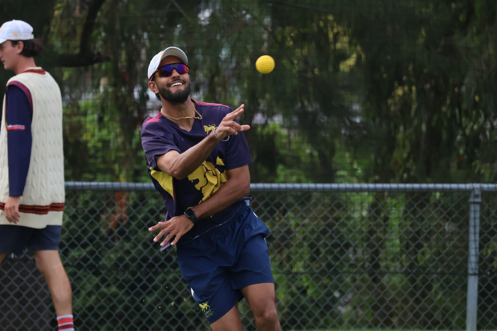 Person in sunglasses catches a yellow ball on a grassy field near a chain-link fence.