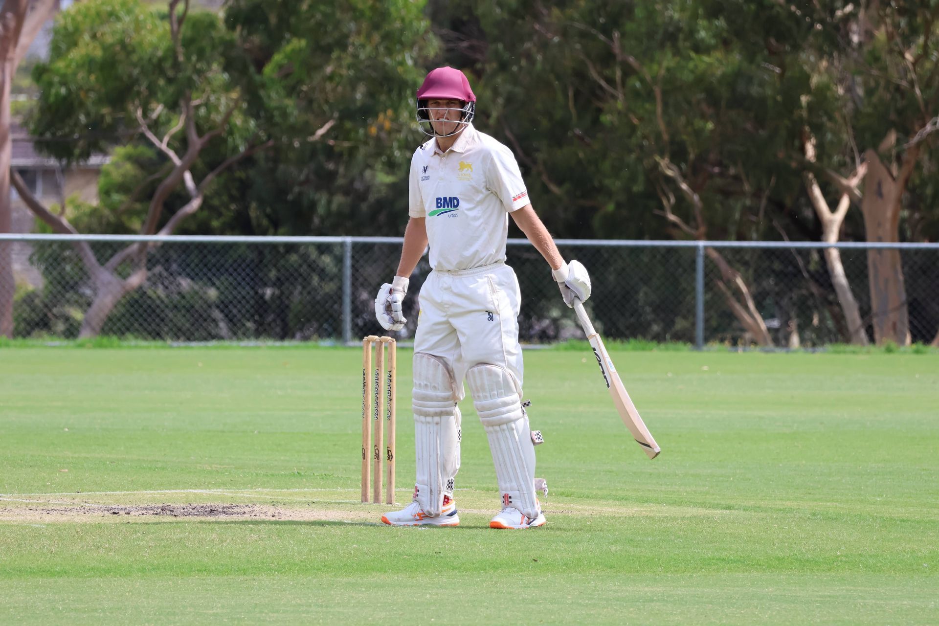 Cricket batsman in white gear and pink helmet standing at the crease on a grassy field