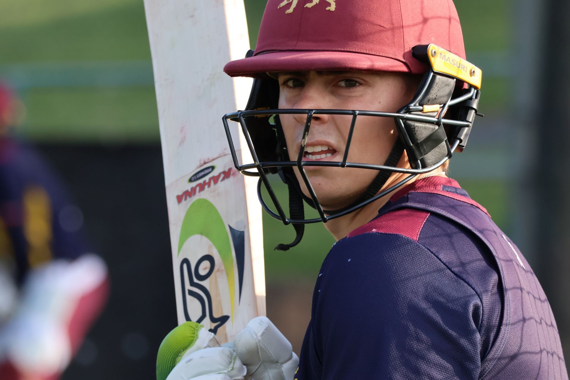 Cricket batter in maroon helmet holding a bat and looking toward the field