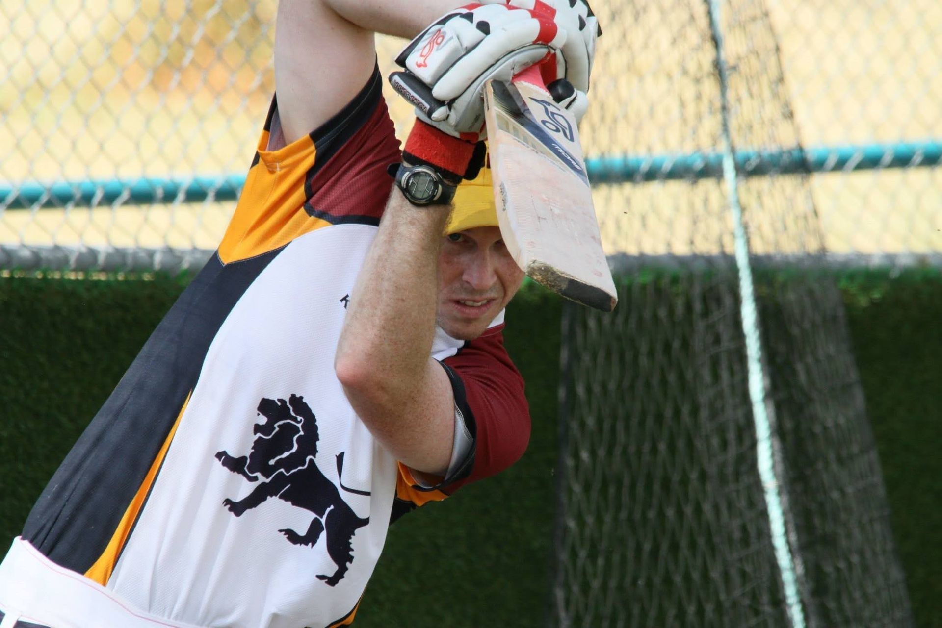 Cricket player in white and maroon uniform holding a bat in a batting stance on the field