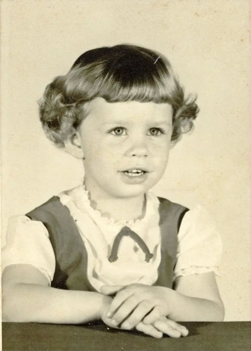 A little girl is sitting at a table in a black and white photo.