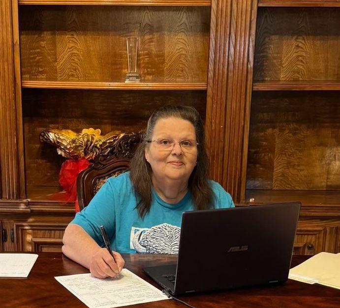 A woman is sitting at a desk in front of a laptop computer.