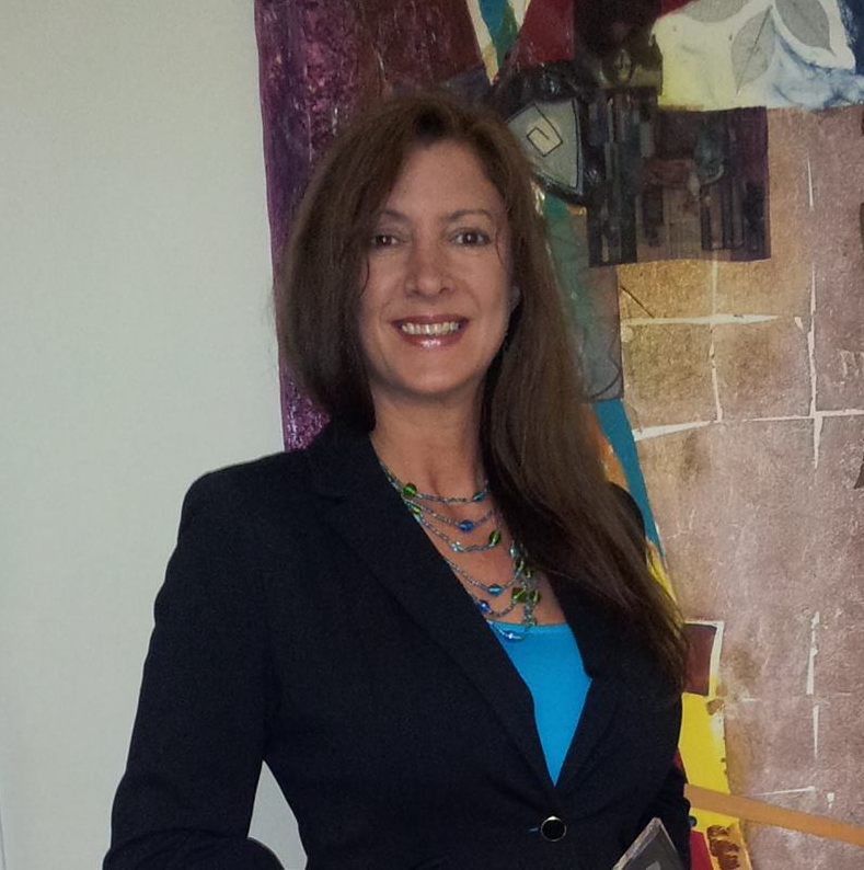 A woman wearing a blue shirt and a black jacket smiles in front of a painting