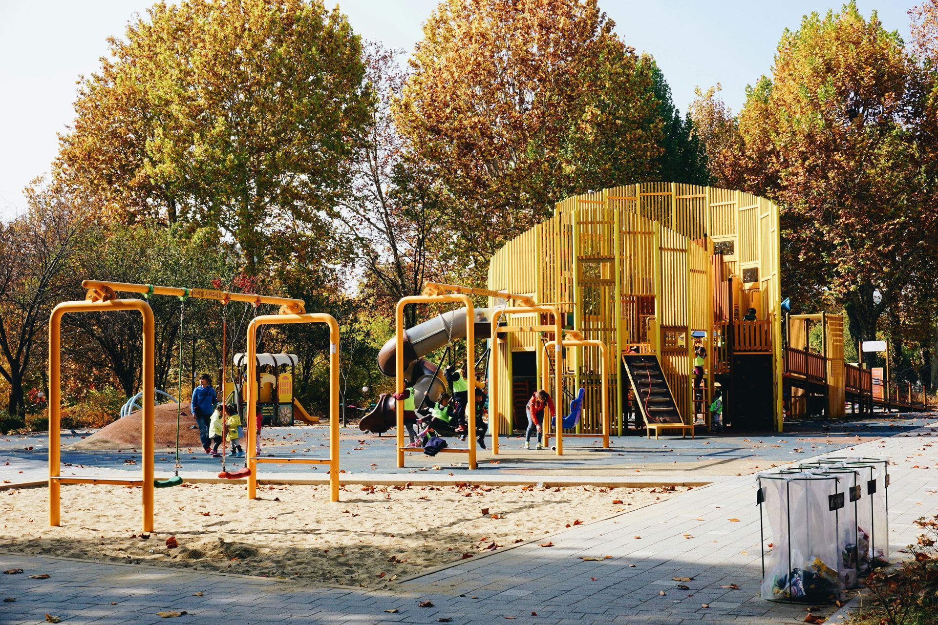A playground with a slide and swings in a park with trees in the background.