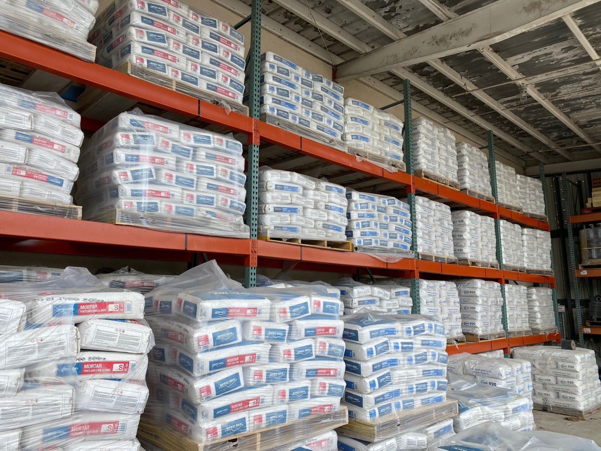 Pallets of mortar and cement mix bags stacked on warehouse shelves for masonry supply.