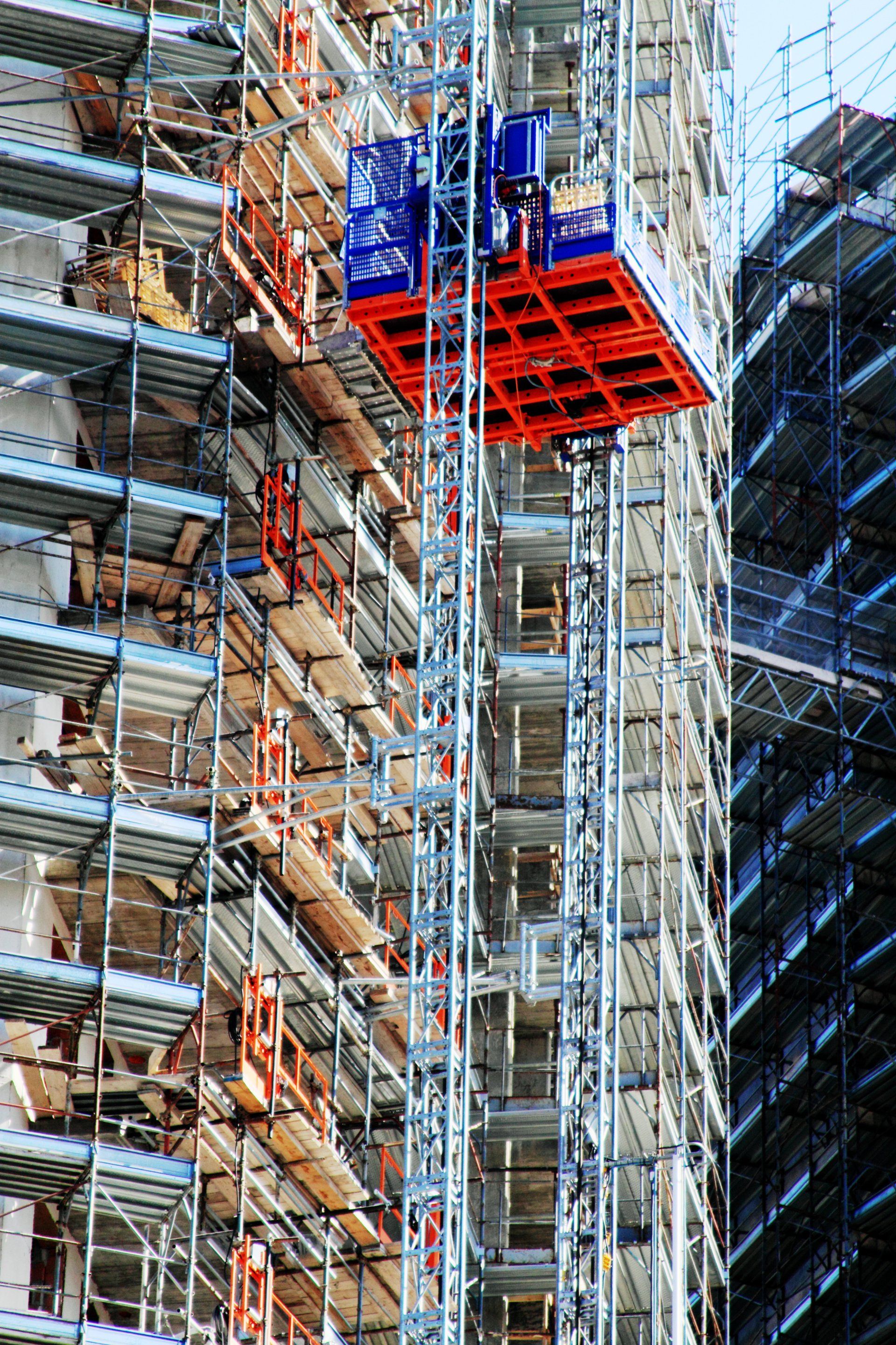 Mast climber scaffolding platform operating on high-rise construction project.
