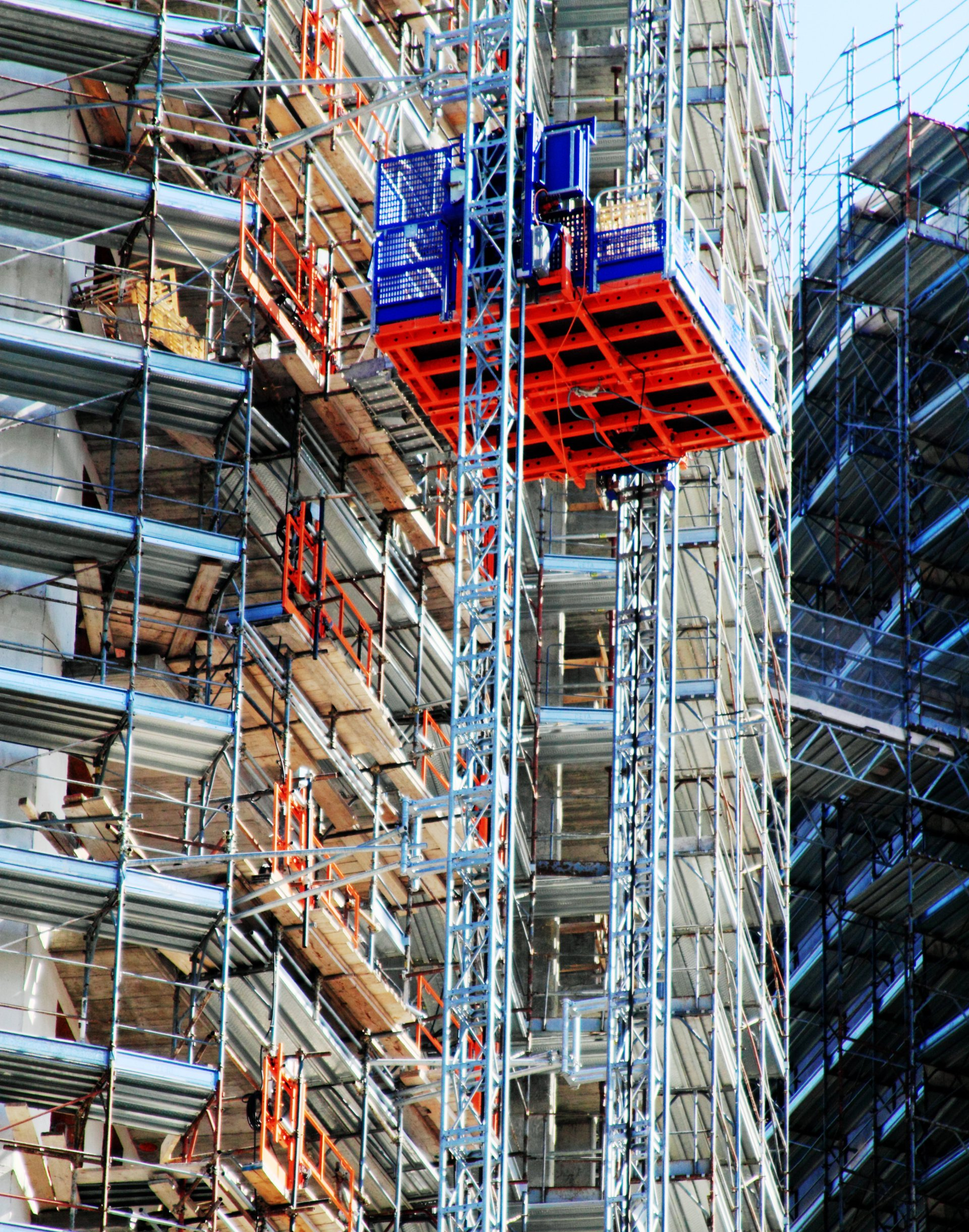 Mast climber scaffolding platform operating on high-rise construction project.