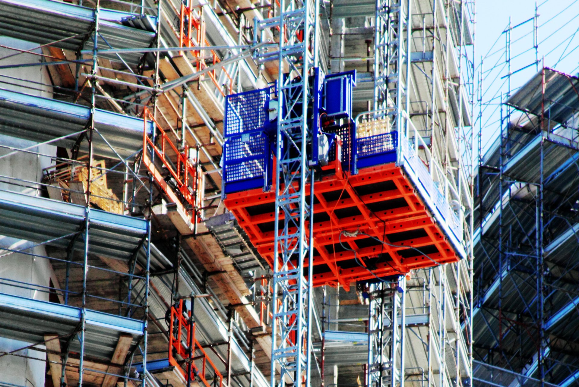 Mast climber scaffolding platform operating on high-rise construction project.