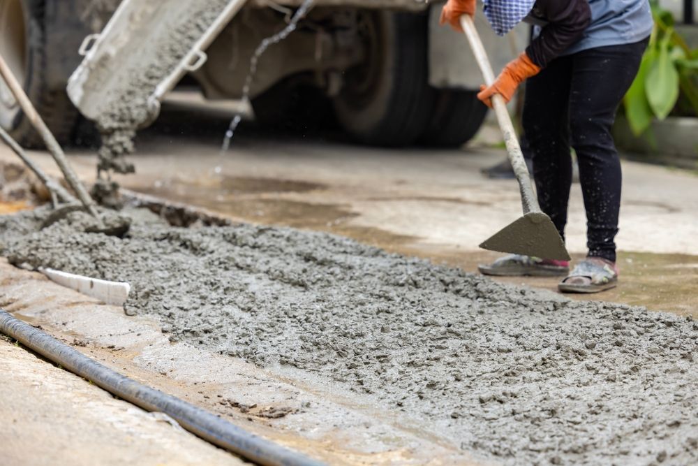 Worker using heavy equipment to spread freshly poured concrete on jobsite.