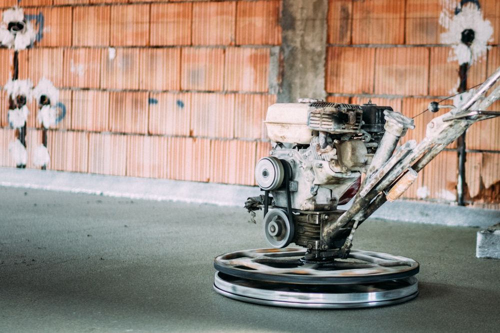 Floor grinder machine on a concrete surface in front of an orange wall with bullet-like marks