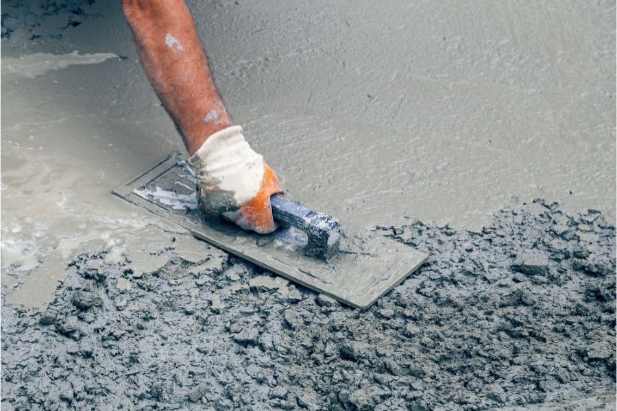 Worker smoothing wet concrete with a hand trowel during slab finishing.