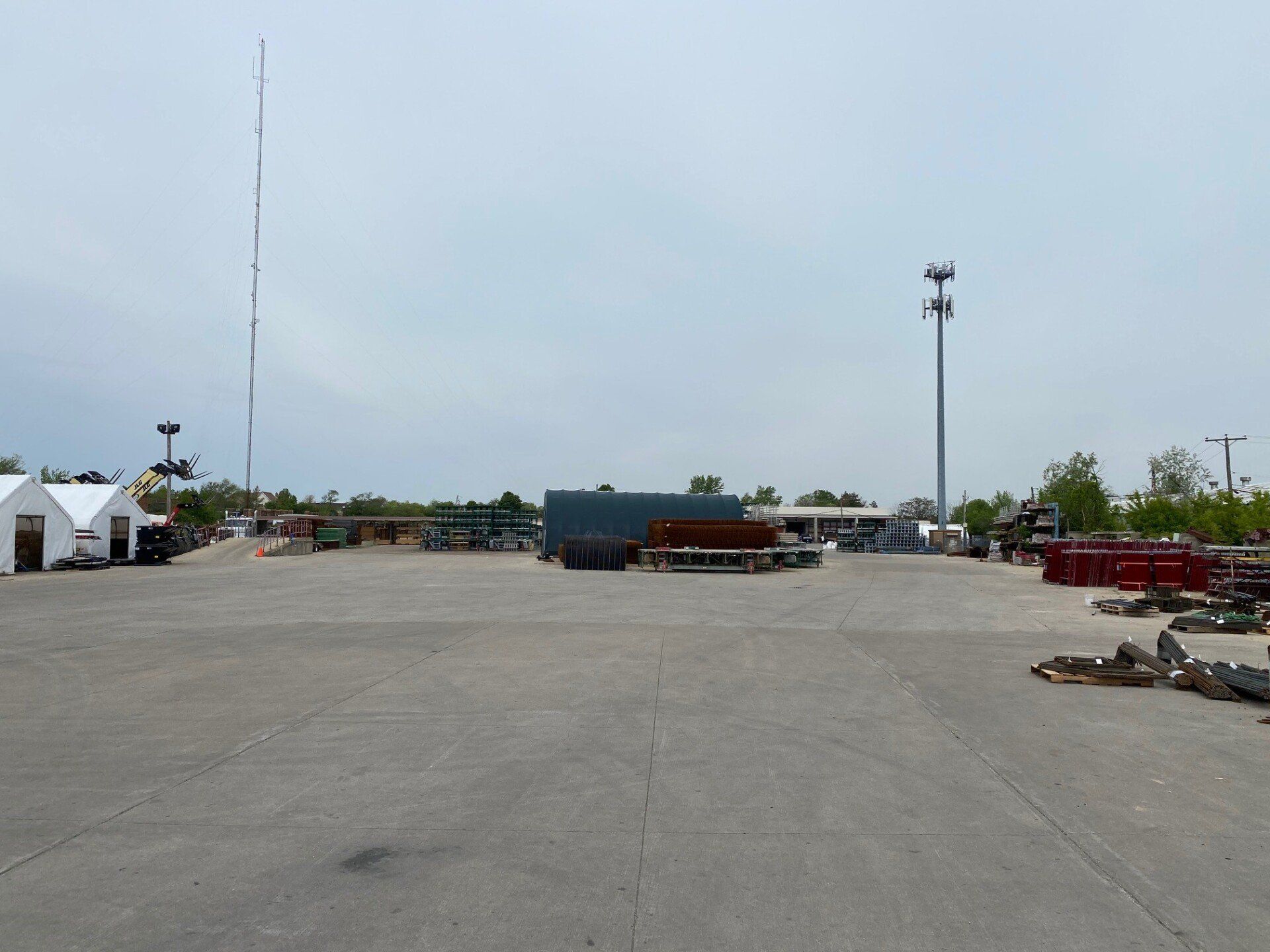 Large outdoor construction equipment yard with concrete forms, scaffolding materials, and rental inventory staged on site