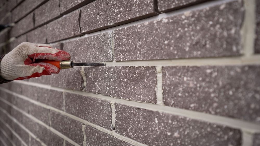 Gloved hand applying red mortar to a gray brick wall