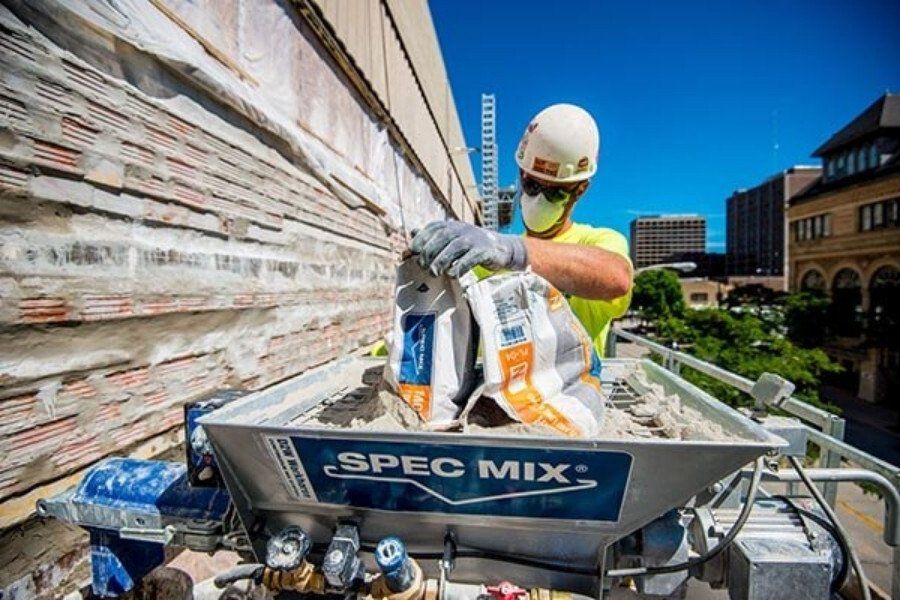 Construction worker loading SPEC MIX materials into mortar mixer on building site.