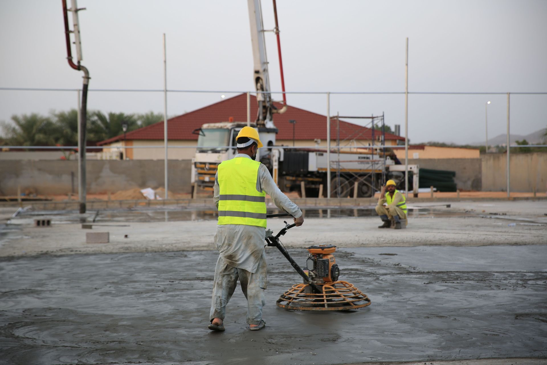 Construction workers using power trowels on a concrete slab at a building site