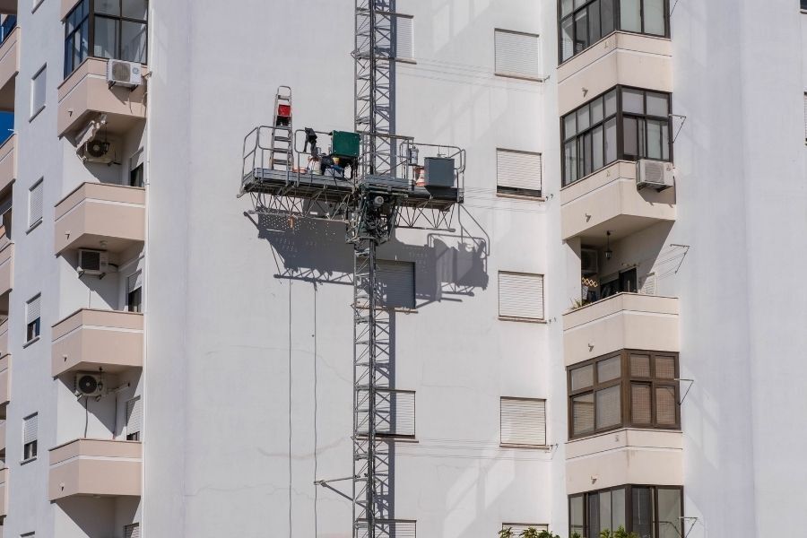 Mast climber platform raised on building exterior for façade and construction work.
