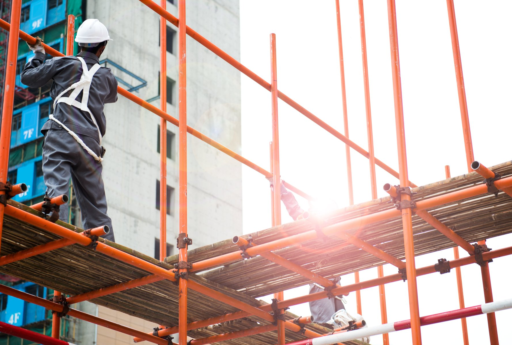Construction workers assembling scaffolding with safety gear at a building site.