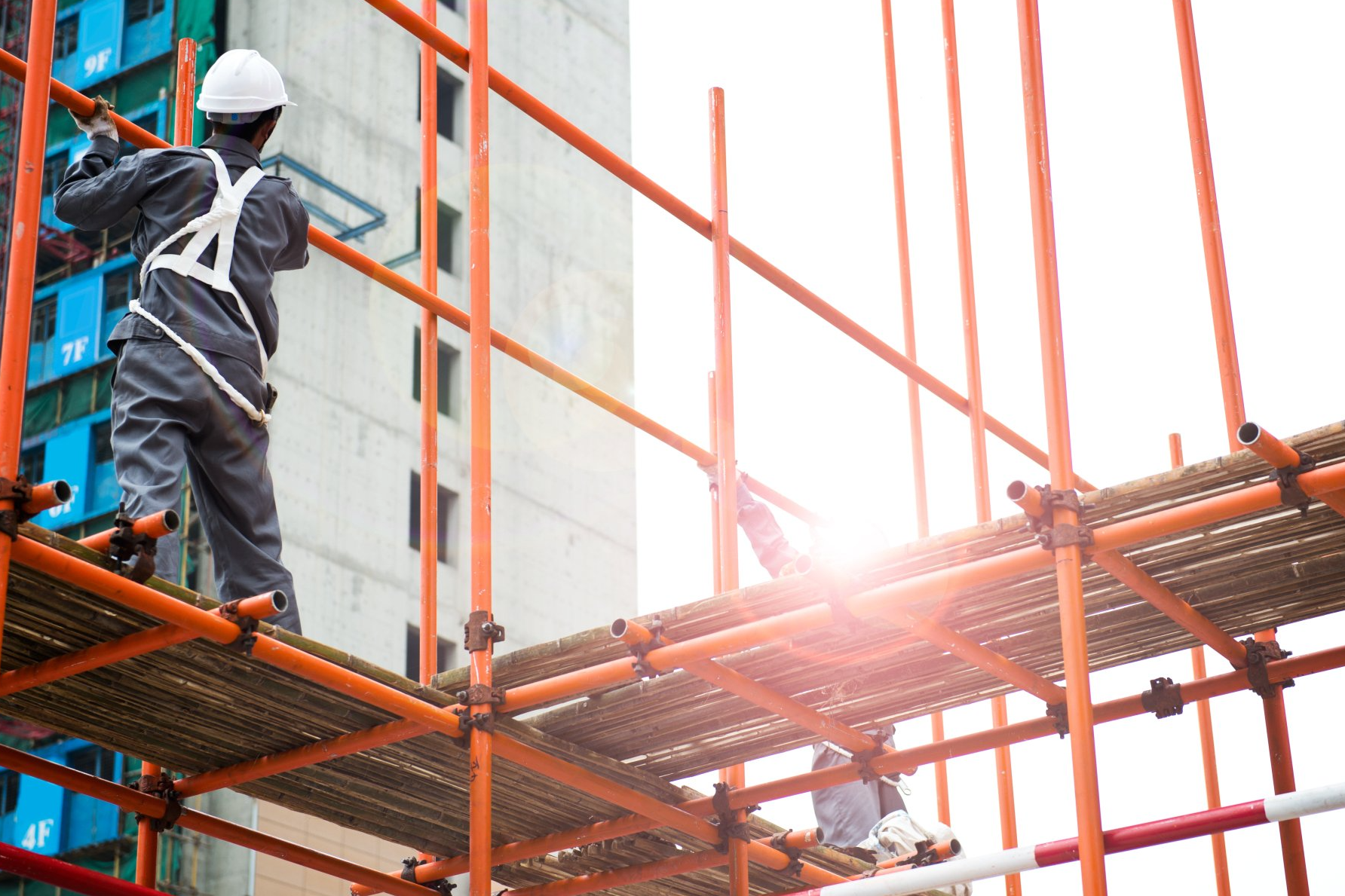 Construction workers assembling scaffolding with safety gear at a building site.