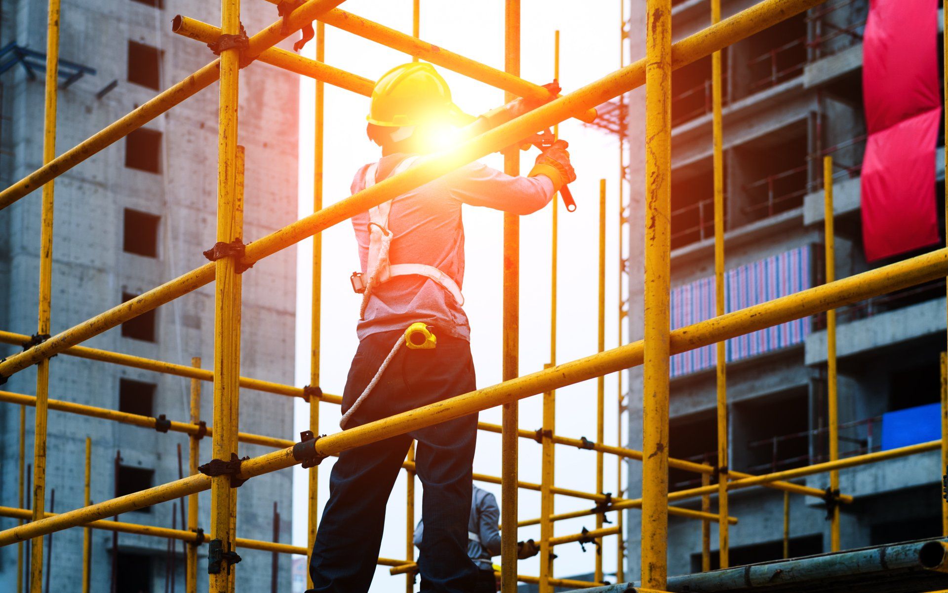Construction worker assembling scaffolding on a multi-story building with safety gear and harness in use