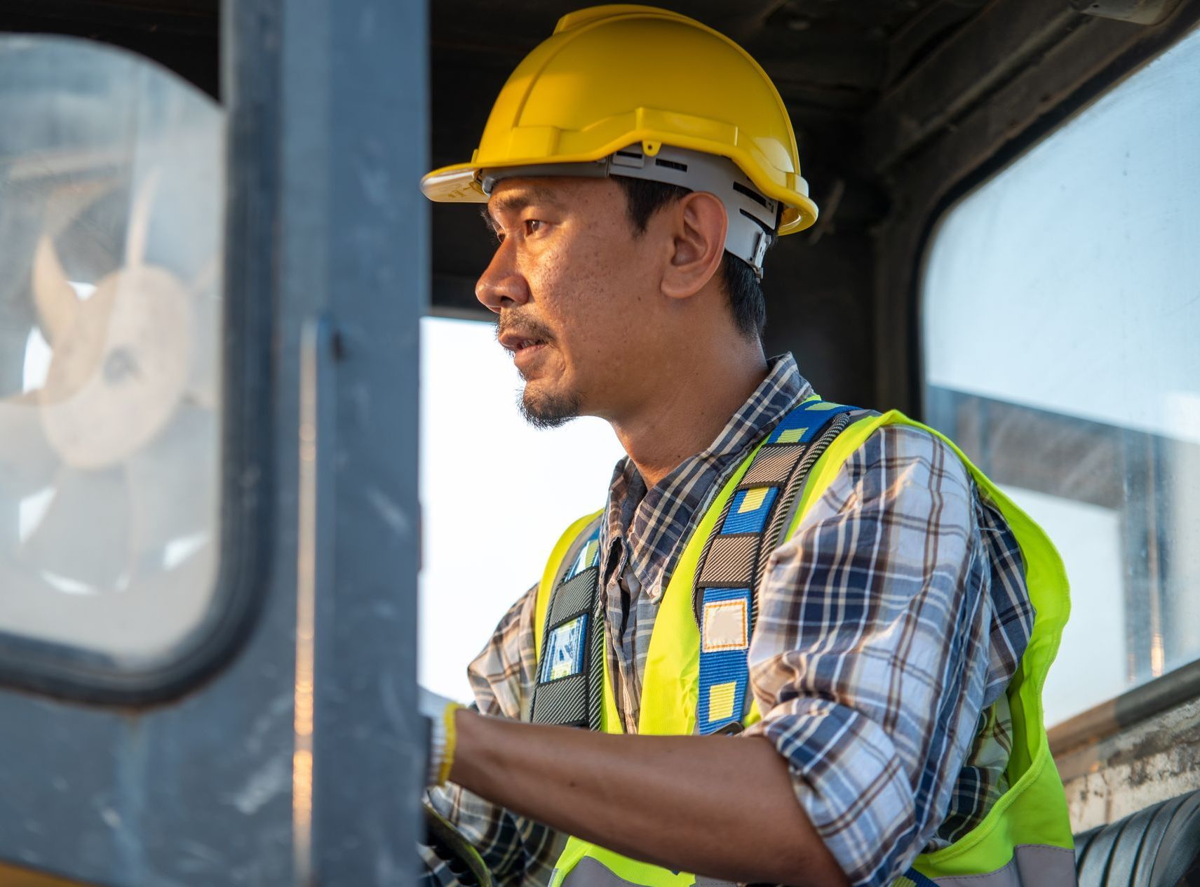 a man wearing a hard hat and safety vest is driving a vehicle 
