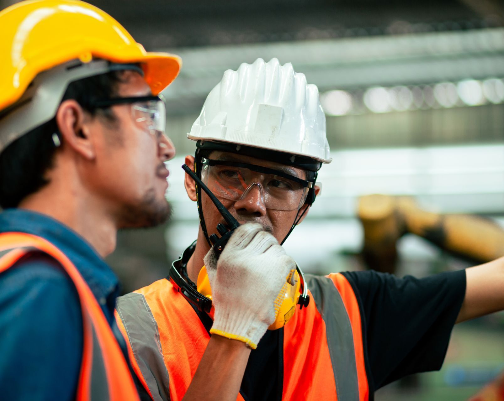 two men wearing hard hats and safety vests are talking on walkie talkies about construction safety