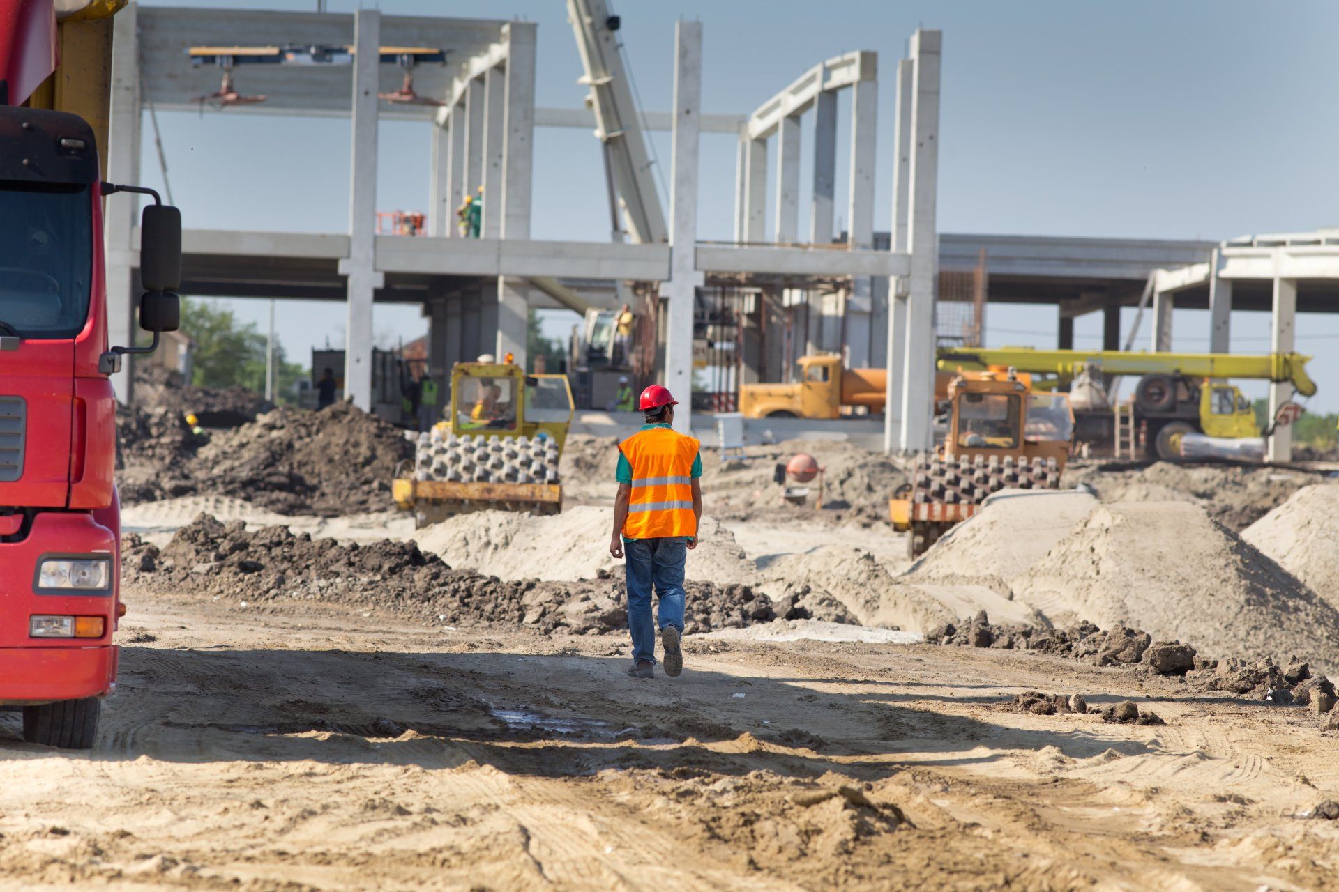 Worker in safety vest overseeing heavy equipment operations at an active construction site.