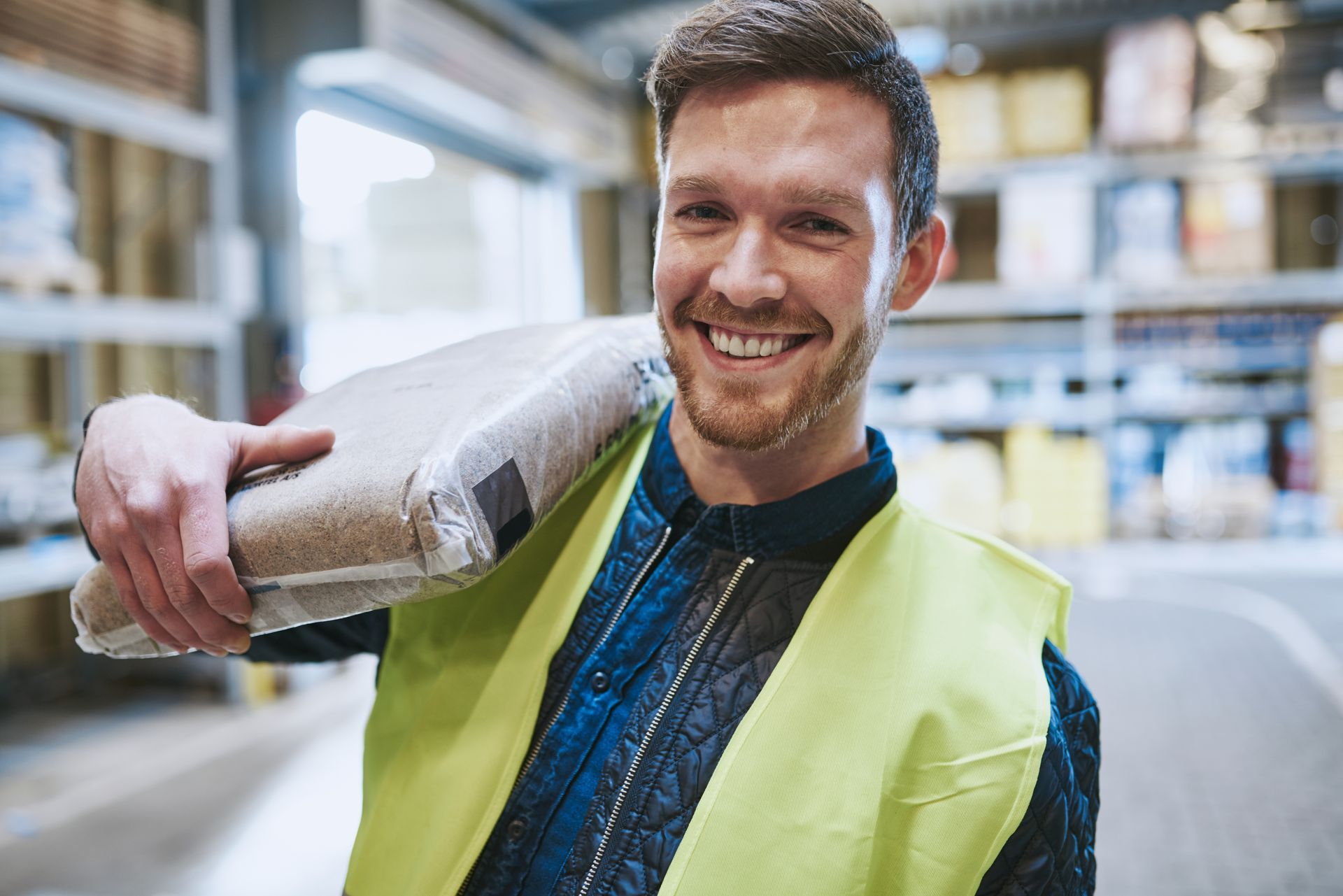 The same young man is carrying a bag of dry, powdered concrete over his shoulder from a local building materials supplier