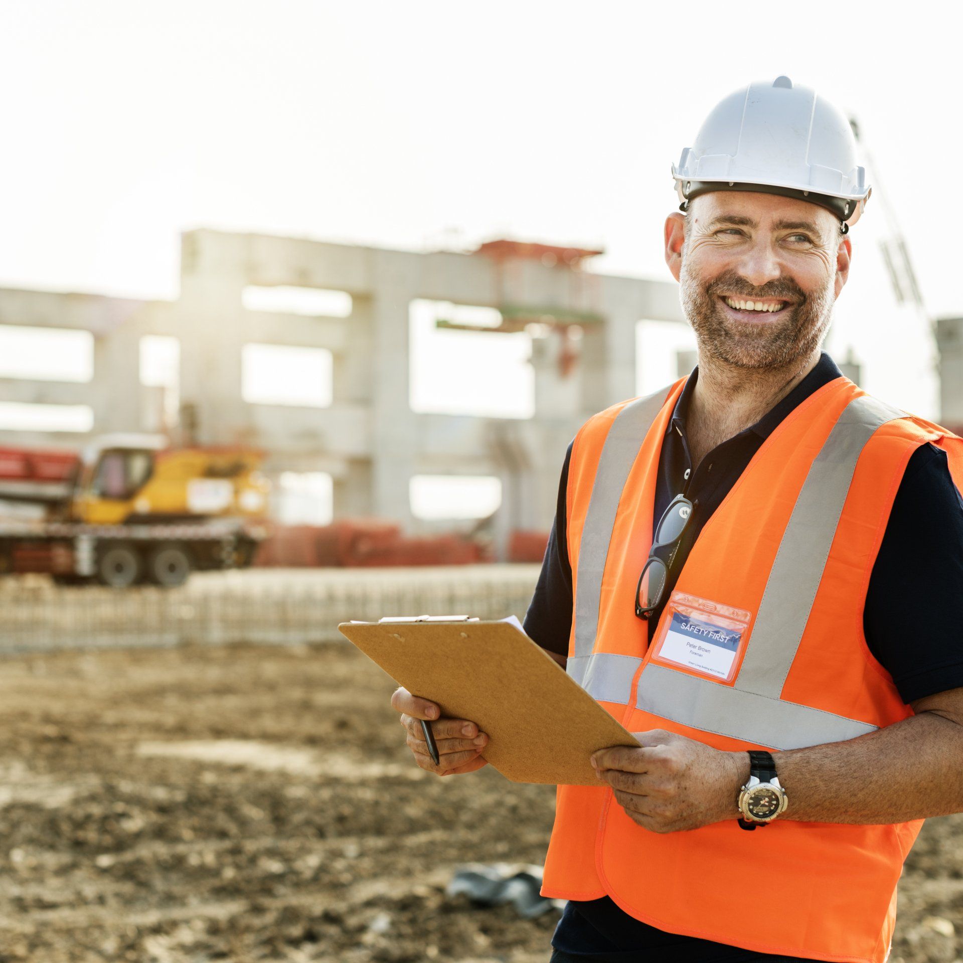 Smiling construction supervisor wearing safety gear reviewing plans on an active commercial construction site