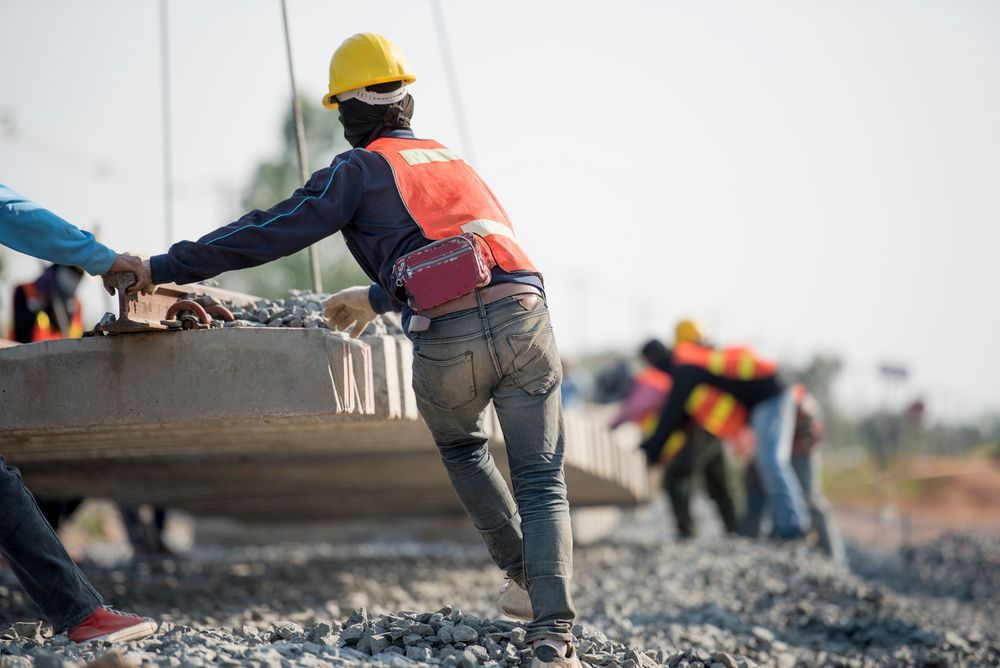 A construction worker is moving a concrete slab along with other construction workers.