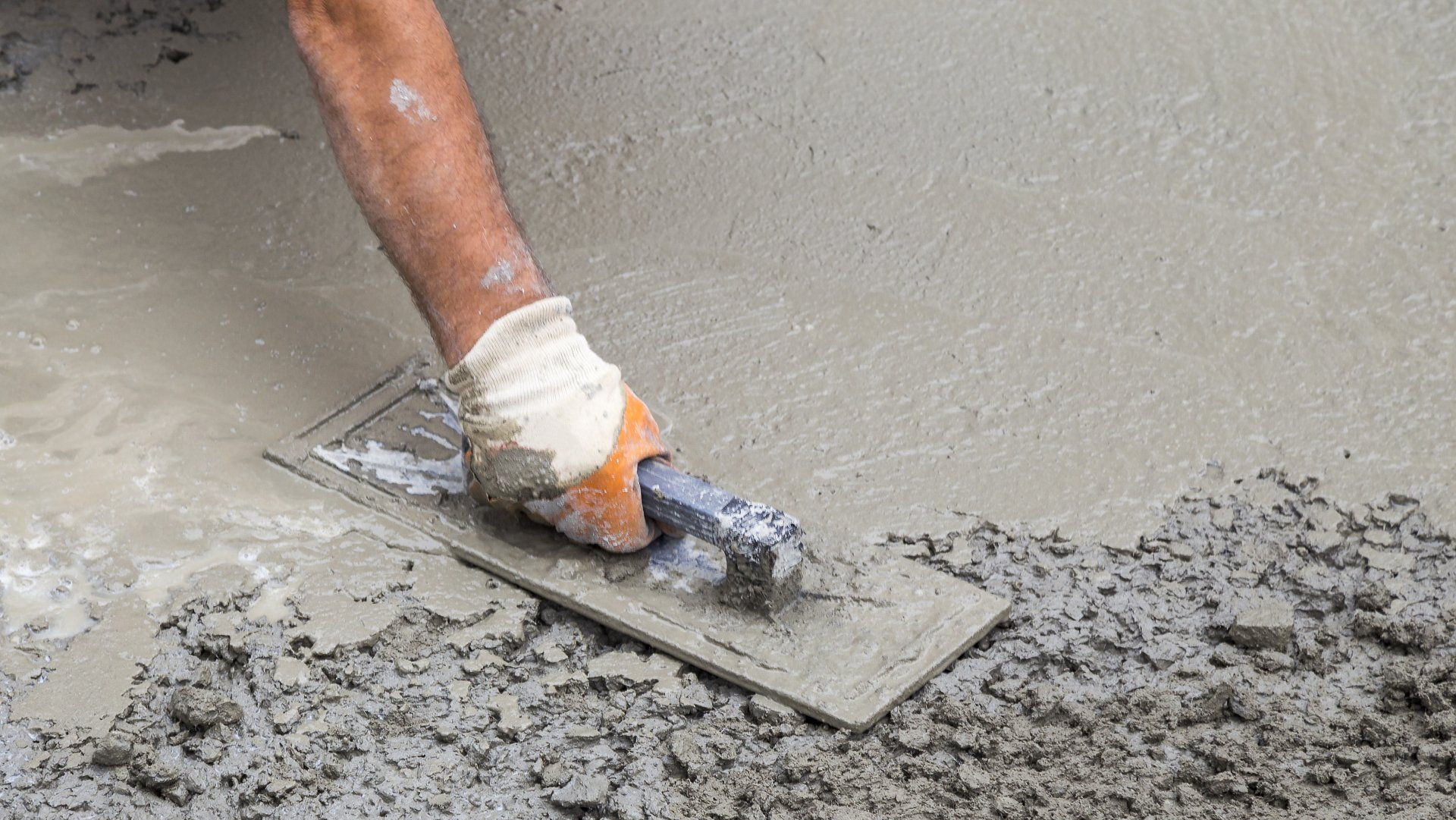 Worker finishing fresh concrete with a hand trowel during slab surface smoothing process