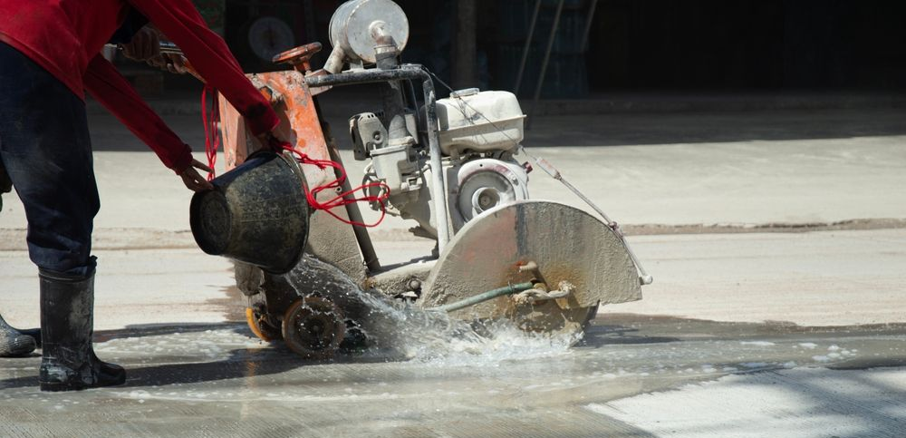 Worker using a concrete saw, cutting pavement with water spraying on the ground