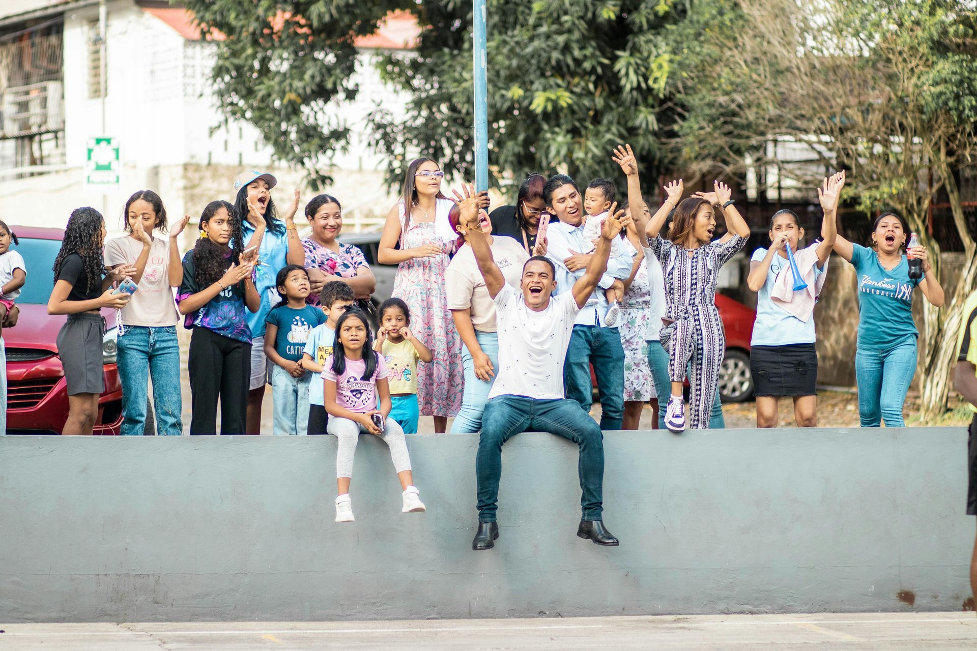 People cheering, some with arms raised, on a concrete barrier outdoors.