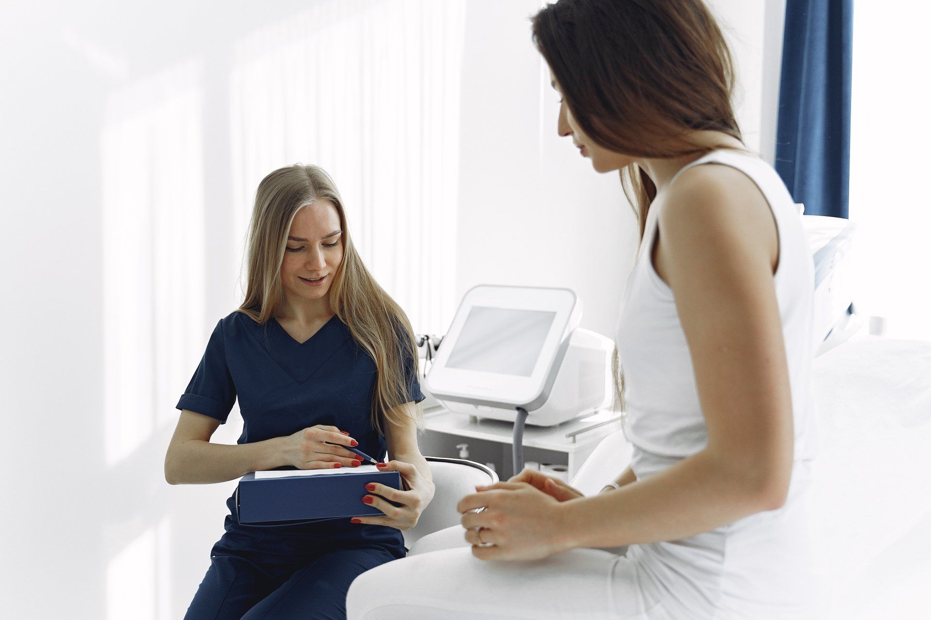 A healthcare professional in blue scrubs consults with a patient in a bright room.