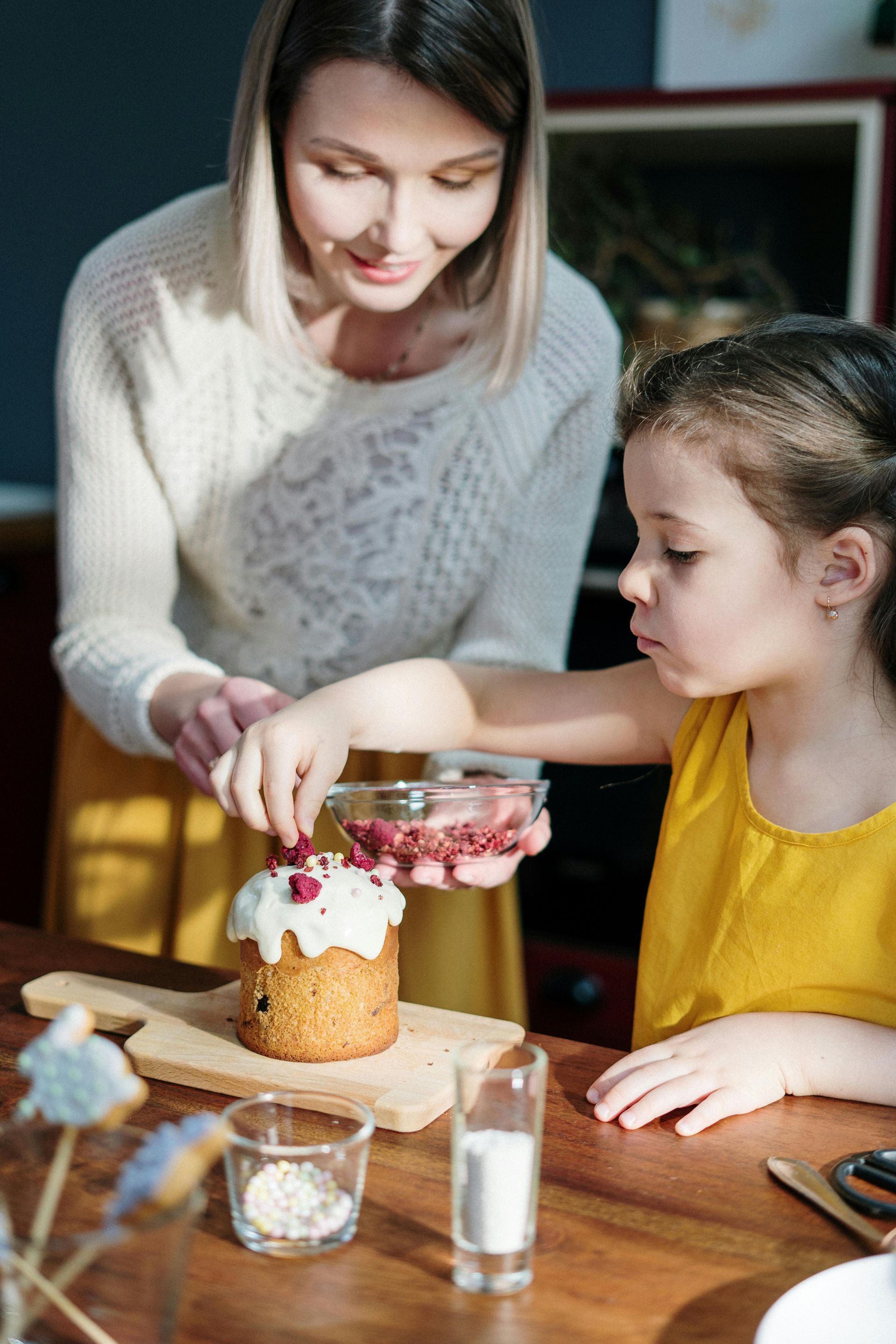 Woman and child decorating cake with berries at a table.