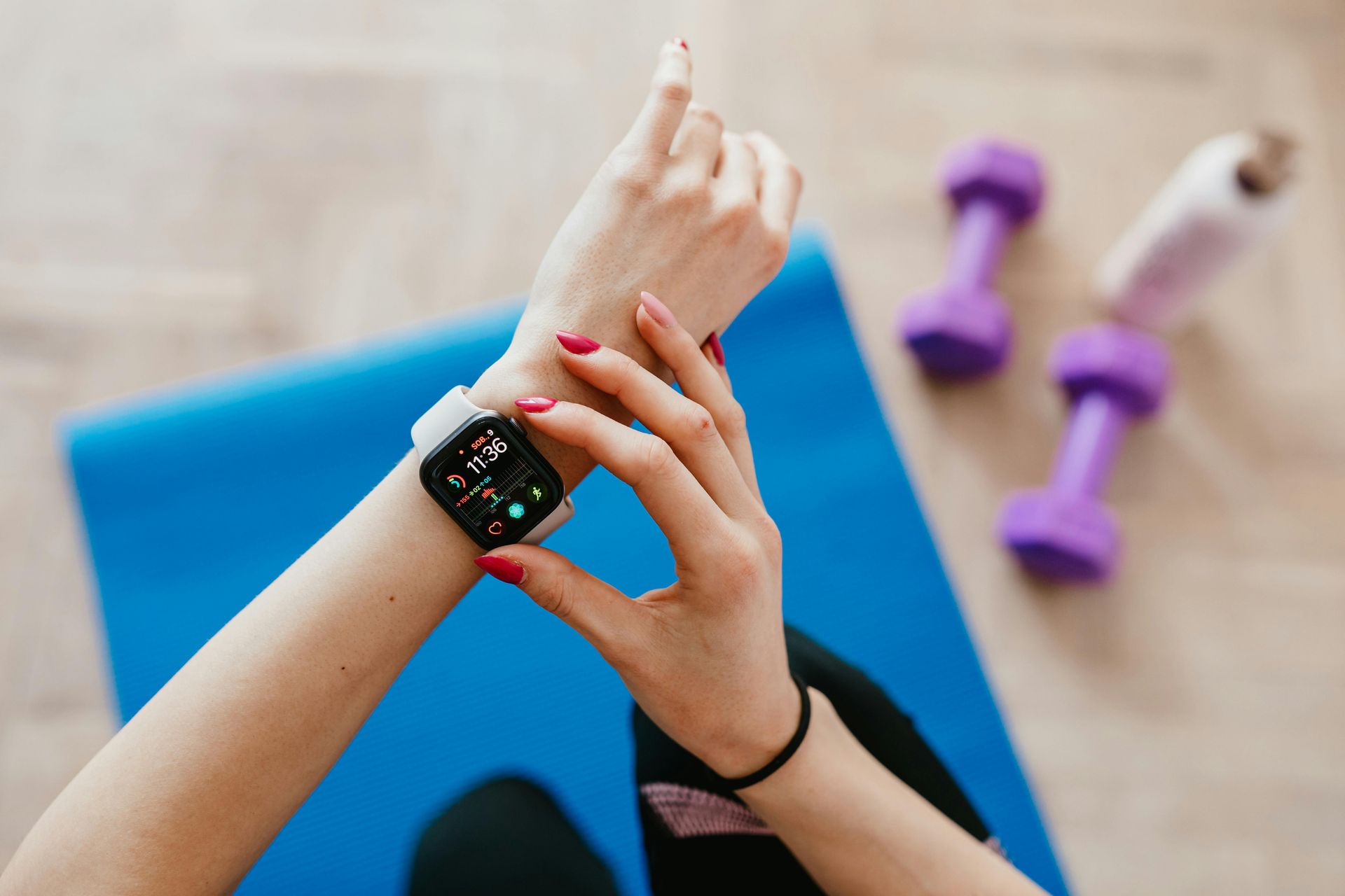 Person checking smartwatch on wrist, with weights and mat.