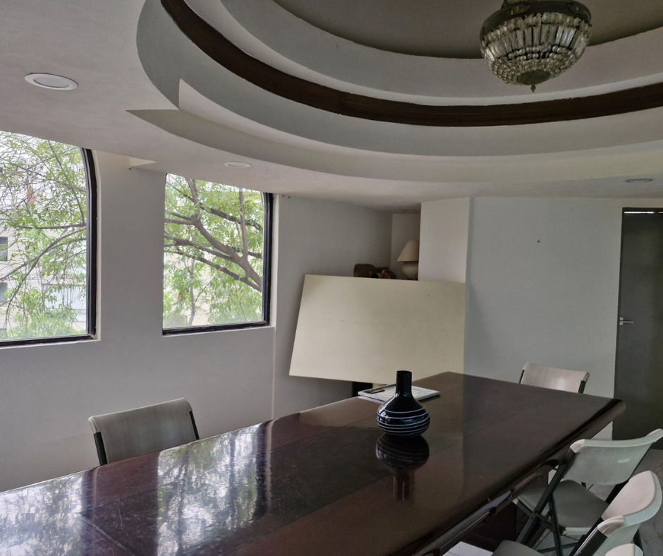 Sala de conferencias con mesa larga y oscura, ventanas con árboles y techo decorativo.